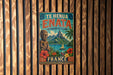 A vintage-style metal sign with a tropical island landscape and a statue, mounted on a wooden wall.