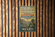 A vintage-style metal sign with text and illustrations of a desert landscape, mounted on a wooden wall.