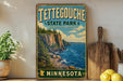A vintage-style metal sign for Tettegouche State Park in Minnesota, featuring a scenic landscape with a cliff overlooking the ocean.