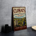 a vintage-style sign for "The Climats" wine, which is a French wine region. The sign displays a landscape with vineyards and a monument, and it is placed on a table next to some black camera lenses.