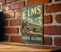 A vintage-style metal sign with the text "The Elms" and "A Gilded Age Treasure" is displayed on a brick wall.