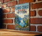 a vintage-style metal sign with a scenic mountain landscape and a small boat on a lake, mounted on a brick wall.
