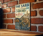 A vintage metal sign with the title "THE SASSI and THE PARK OF THE RUPESTRIAN CHURCHES OF MATERA ITALY" is displayed on a brick wall.