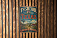 A vintage-style metal sign with the text "THISTLE HILL TEXAS" and a scenic illustration of a rural landscape with a windmill, barn, and flowers.