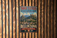 A vintage metal sign with the text "Three Castles and Defensive Wall and Ramparts of the Market-Town of Bellinzona SWITZERLAND" hanging on a wooden wall.