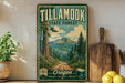 A vintage-style sign for Tillamook State Forest in Oregon, featuring a scenic mountain landscape and a road leading through the forest.