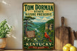 A vintage-style metal sign for Tom Dorman State Nature Preserve in Kentucky, featuring a scenic landscape with a red cardinal perched on a branch.