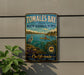 A vintage-style metal sign for Tomales Bay, California, featuring a scenic illustration of a person kayaking in the bay surrounded by lush greenery.