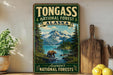 A vintage-style sign for Tongass National Forest in Alaska, featuring a scenic landscape with a bear, mountains, and a river.