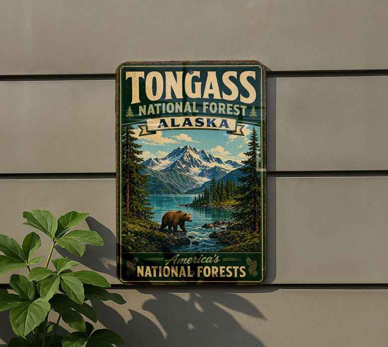 A vintage-style metal sign for Tongass National Forest in Alaska, featuring a scenic landscape with a bear, mountains, and a river.