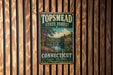 A vintage metal sign for Topmead State Forest in Connecticut, featuring a scenic landscape with a bridge and trees.