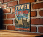A vintage-style sign for the Tower of London, a famous landmark in the United Kingdom, is displayed on a brick wall.