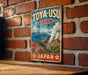 A vintage-style sign for Toya-USU Park, featuring a scenic illustration of a mountainous landscape with a volcano and flowers.