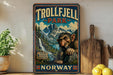 a vintage-style sign for Trollfjell Park in Norway, with a large illustration of a gnome-like creature in the foreground. The sign is displayed on a wooden shelf, surrounded by various kitchen items such as a cutting board, a lemon, and a potted plant.