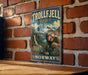 A vintage-style metal sign for Trolljell Park in Norway, featuring a whimsical illustration of a gnome-like creature in a natural landscape.