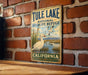 A vintage-style metal sign for Tule Lake National Wildlife Refuge in California, featuring a white goose and a serene landscape.