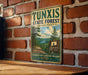 A vintage-style sign for Tunxis State Forest in Connecticut, featuring a scenic landscape with pine trees and a river.