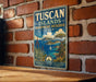 A vintage-style metal sign with the text "TUSCAN ISLANDS BIOSPHERE RESERVE ITALY" is displayed on a brick wall.