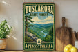 A vintage-style metal sign for Tuscarora State Forest in Pennsylvania, featuring a scenic mountain landscape with pine trees and a winding river.