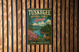 A vintage metal sign for Tuskegee National Forest in Alabama, featuring a scenic landscape with a river, mountains, and wildlife.