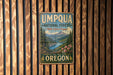 A vintage metal sign for the Umpqua National Forest in Oregon, featuring a scenic mountain landscape with a river and pine trees.