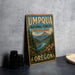 A vintage-style metal sign for the Umpqua National Forest in Oregon, featuring a scenic landscape with mountains, pine trees, and a river.