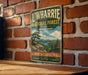A vintage-style metal sign for Uwharrie National Forest, featuring a scenic landscape with mountains, pine trees, and a lake.