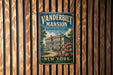 A vintage-style metal sign for the Vanderbilt Mansion, a historic site in New York, is displayed on a wooden wall.