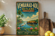 A vintage-style metal sign advertising Vembanad-Kol Wetland, a famous natural wonder in Kerala, India. The sign features a tropical landscape with palm trees, a river, and a boat on the water.