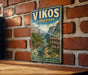 A vintage-style metal sign for Vikos Park in Greece, featuring a scenic mountain landscape with a river and bridge.