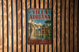 A vintage-style poster advertising the Villa Adriana in Italy, featuring a classical architectural scene with a fountain and statues.