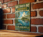 A vintage-style metal sign for Waccassass Bay Preserve, Florida, featuring a serene landscape with palm trees, a manatee, and a body of water.