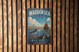 A vintage metal sign with a nautical scene, featuring a lighthouse, a boat, and birds, is displayed on a wooden wall.