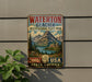A vintage-style metal sign advertising Waterton Glacier International Peace Park, featuring a scenic mountain landscape with a lake and buildings.