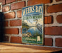 A vintage-style metal sign for Weeks Bay National Estuarine Research Reserve in Alabama, featuring an illustration of a bird and a body of water.