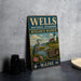 A vintage metal sign for the Wells National Estuarine Research Reserve in Maine, featuring a seagull and a lighthouse, is displayed on a gray countertop next to some black camera lenses.