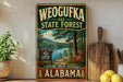 A vintage-style metal sign for Weoguffee State Forest in Alabama, featuring a scenic landscape with a lake and pine trees.