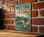 A vintage-style metal sign for West Lake, a cultural landscape in Hangzhou, China, featuring a scenic image of a traditional Chinese boat on a lake.