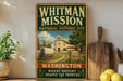 A vintage-style sign for the Whitman Mission National Historic Site, featuring an illustration of a historic building and wagon, with the text "WHITMAN MISSION" and "NATIONAL HISTORIC SITE" prominently displayed.