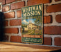 A vintage-style metal sign for the Whitman Mission Historic Site, featuring an illustration of a historic building and a wagon, mounted on a brick wall.