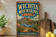 A vintage-style sign for the "Wichita Mountains Trail" in Oklahoma, featuring a scenic landscape with mountains, a river, and desert vegetation.