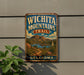 A vintage-style metal sign with the text "WICHITA MOUNTAINS TRAIL" and "OKLAHOMA" printed on it, mounted on a wall next to a plant.
