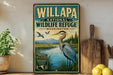 A vintage-style metal sign for Willapa National Wildlife Refuge in Washington, featuring an illustration of a bird standing on a grassy bank overlooking a river.