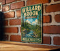 A vintage metal sign for Willard Brook State Forest in Massachusetts, featuring a scenic illustration of a forest and a river.