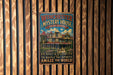 A vintage metal sign for the Winchester Mystery House in San Jose, California, featuring an illustration of the house and the text "Built in Mystery to Baffle the Spirits Amaze the World!"