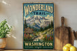 A vintage-style metal sign with a mountain landscape and trail sign, advertising the Wonderland Trail in Washington.
