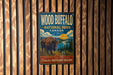 A vintage-style metal sign for Wood Buffalo National Park in Canada, featuring an illustration of a bison in a grassy field with a lake and mountains in the background.