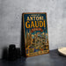 A vintage metal sign with the text "WORKS OF ANTONI GAUDI SPAN" and an illustration of the Sagrada Familia, a famous Barcelona cathedral, is displayed on a gray countertop.