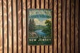 A vintage metal sign for Worthington State Forest in New Jersey, featuring a scenic landscape with pine trees, a lake, and mountains.