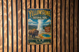 A vintage-style metal sign for Yellowstone National Park, featuring an illustration of a bison and a geyser, mounted on a wooden wall.